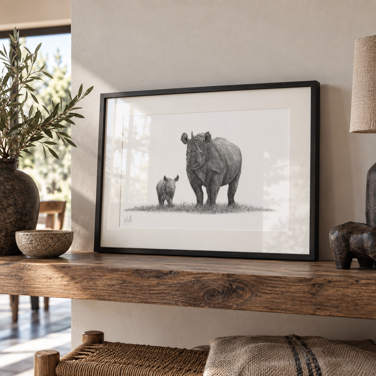 African Black Rhino mother and calk pencil drawing in a black wood frame standing on a shelf against a beige wall with ornaments and plants on the shelf