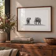 A framed black and white elephant art print hangs on a beige wall above a rustic wooden console table styled with a vase, books, and a lamp.