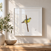 A framed art print of an African Green Pigeon perched on a branch, displayed on a light beige wall above a wooden console table with a vase and bowl.