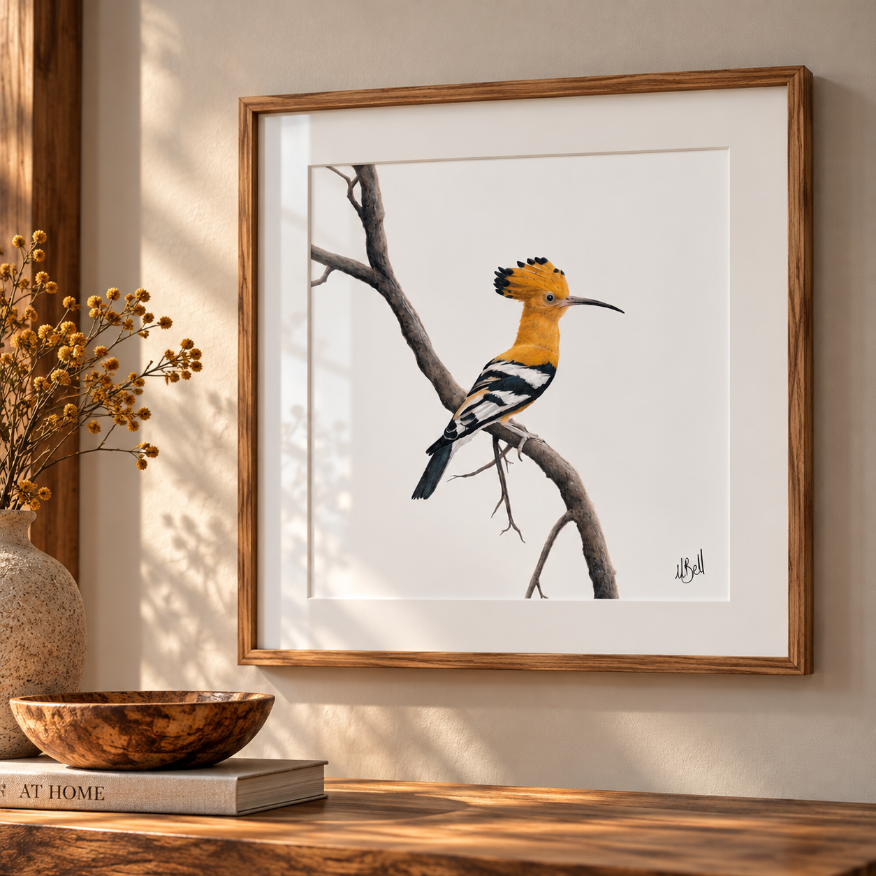 Framed wall art featuring a pencil drawing of an African Hoopoe bird perched on a branch, displayed in a warm wood frame on a beige wall above a wooden surface with a vase and bowl nearby.