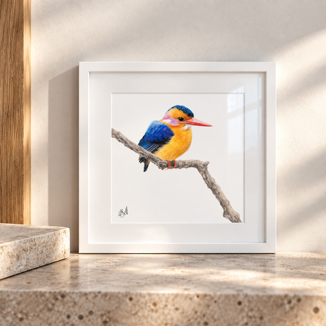 A framed art print of a colorful kingfisher perched on a branch, displayed on a stone ledge against a sunlit beige wall.