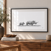A framed black and white rhinoceros art print hangs on a light beige wall above a wooden console table in a styled room setting with books, a plant, and bowls.