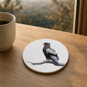 Wooden coaster with white background of a Bateleur, on a light brown wooden table with a mug of coffee next to it