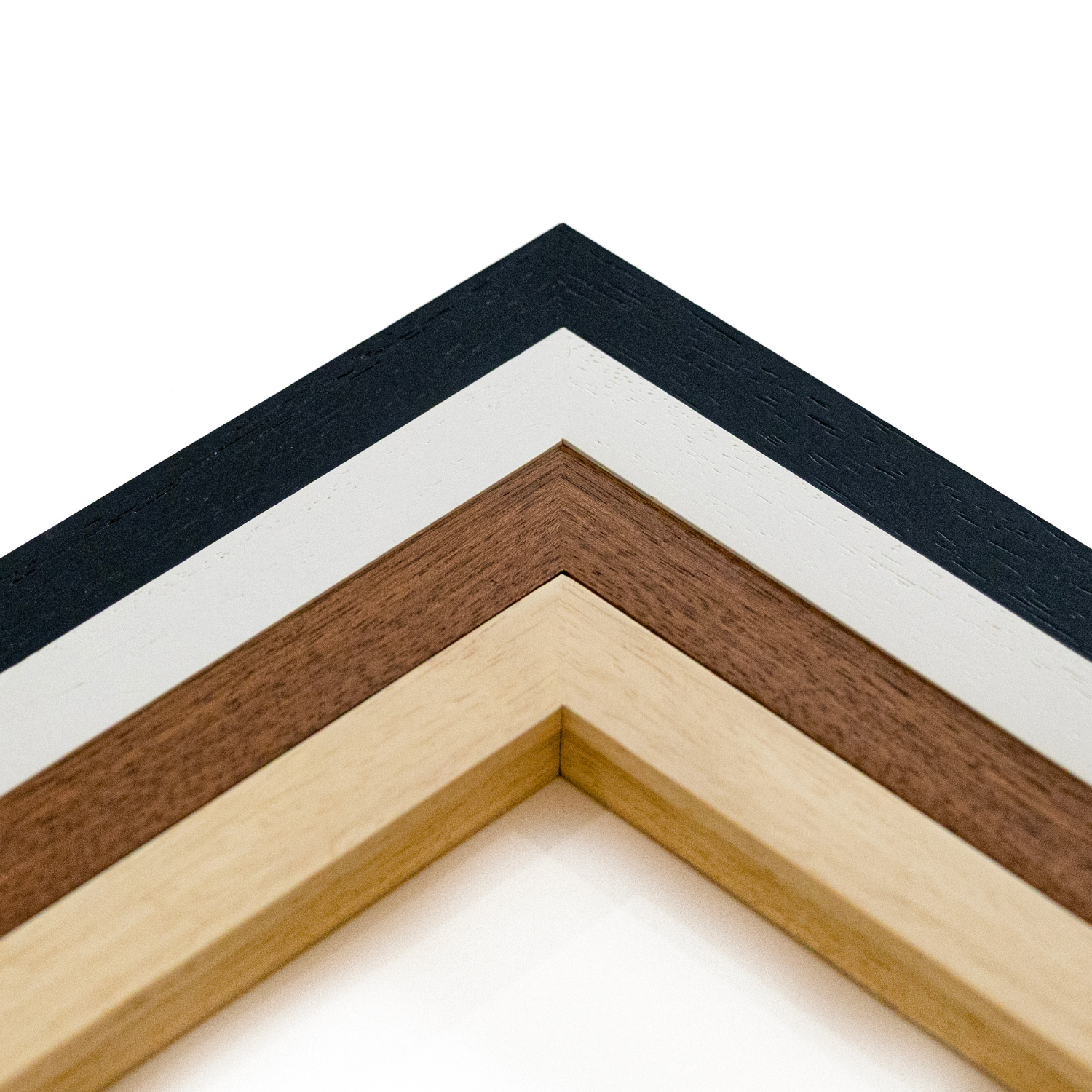Four nested picture frame corners arranged in an inverted V shape, showing different wood tones and a painted finish: black, white, medium brown, and light natural wood, photographed on a white background.