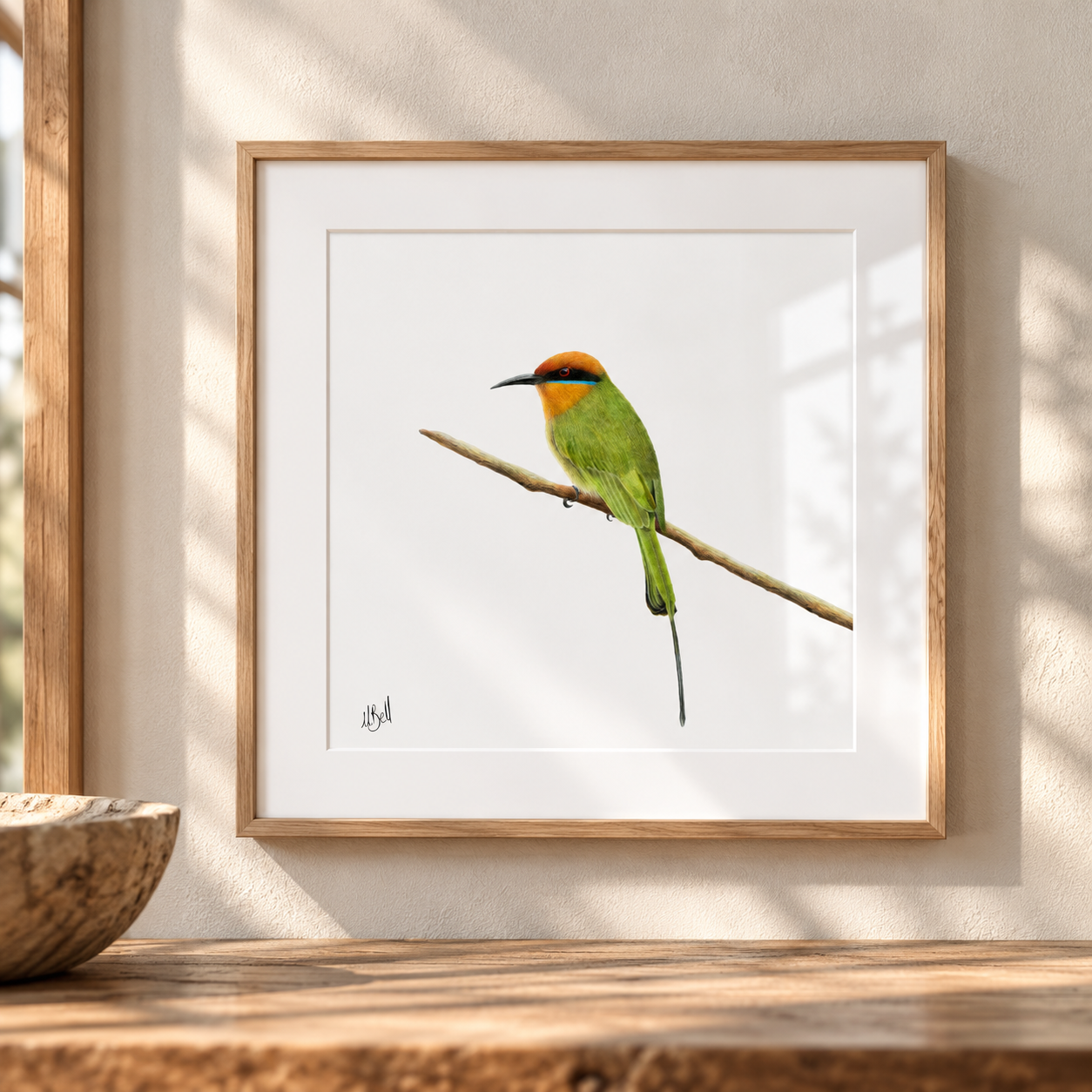 A framed art print of a Bohms Bee-Eater bird with a bright orange-red crown, perched on a branch against a white background, displayed on a wooden shelf in a sunlit room.