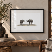 Framed wall art featuring a black-and-white illustration of two buffalo facing each other, displayed on a beige wall above a rustic wooden table with books and a vase.