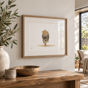 A framed art print of a walking cheetah hanging on a light beige wall above a rustic wooden console table. The print features a detailed watercolor-style illustration of a cheetah on a white mat, enclosed in a light oak wood frame.
