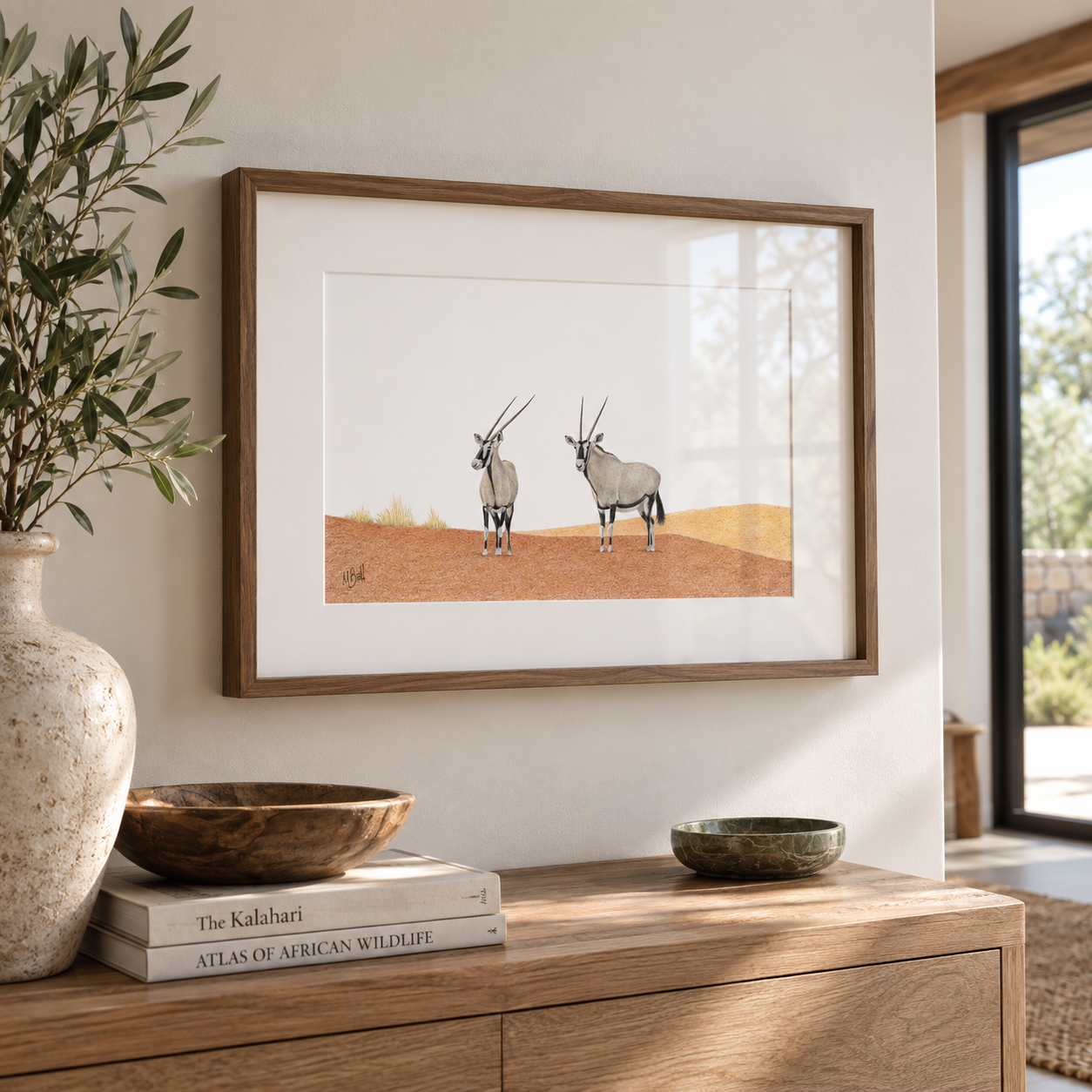 A kiaat framed pencil drawing by Matthew Bell hanging on the wall in a living room above a wooden sideboard with books and flowers