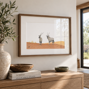 A kiaat framed pencil drawing by Matthew Bell hanging on the wall in a living room above a wooden sideboard with books and flowers