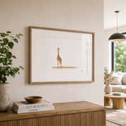A framed art print featuring a detailed illustration of a giraffe standing on a patch of dry grass, displayed on a beige wall above a wooden console table in a modern living room setting.