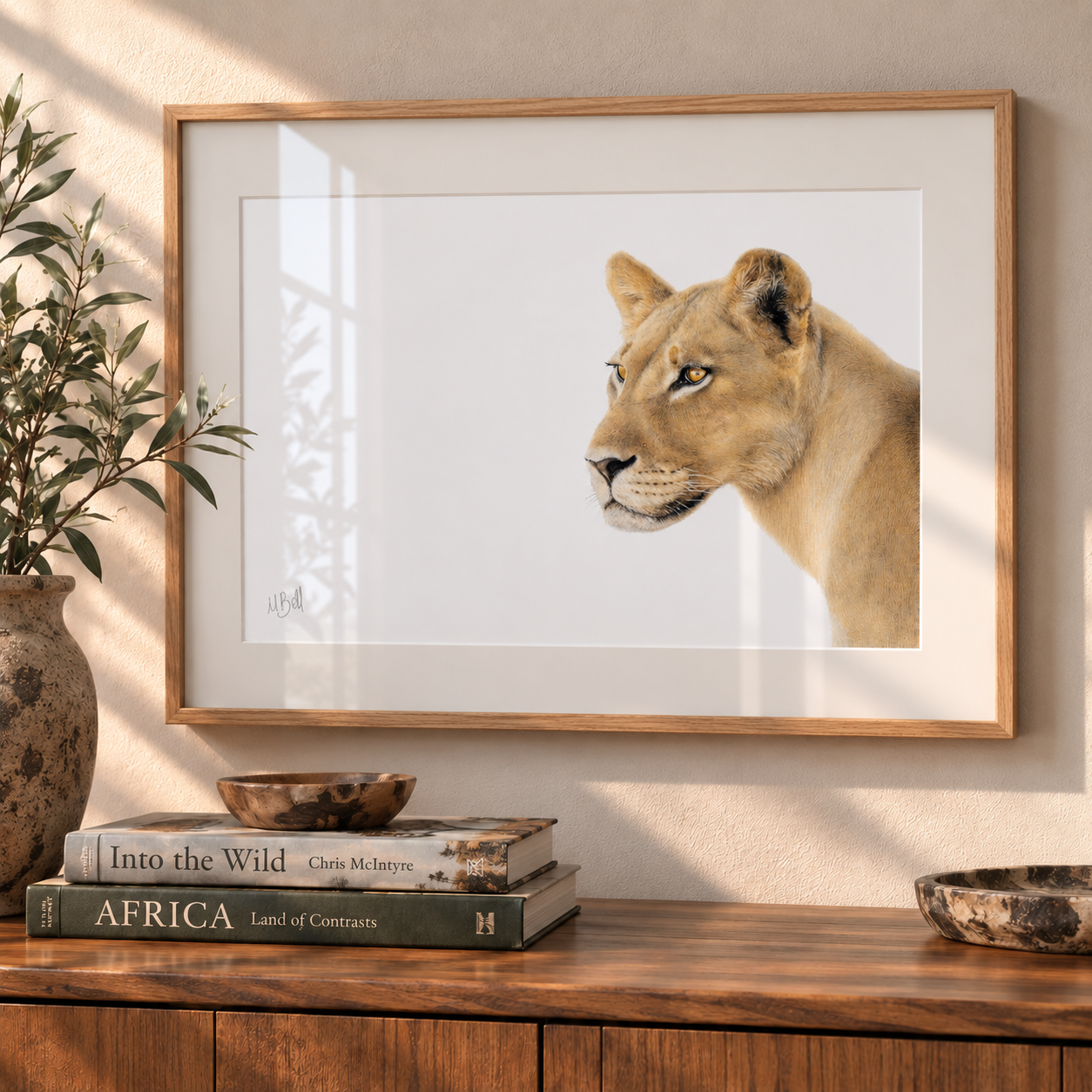 A framed art print of a lioness head portrait hanging on a beige wall above a wooden console table with books and decorative bowls.