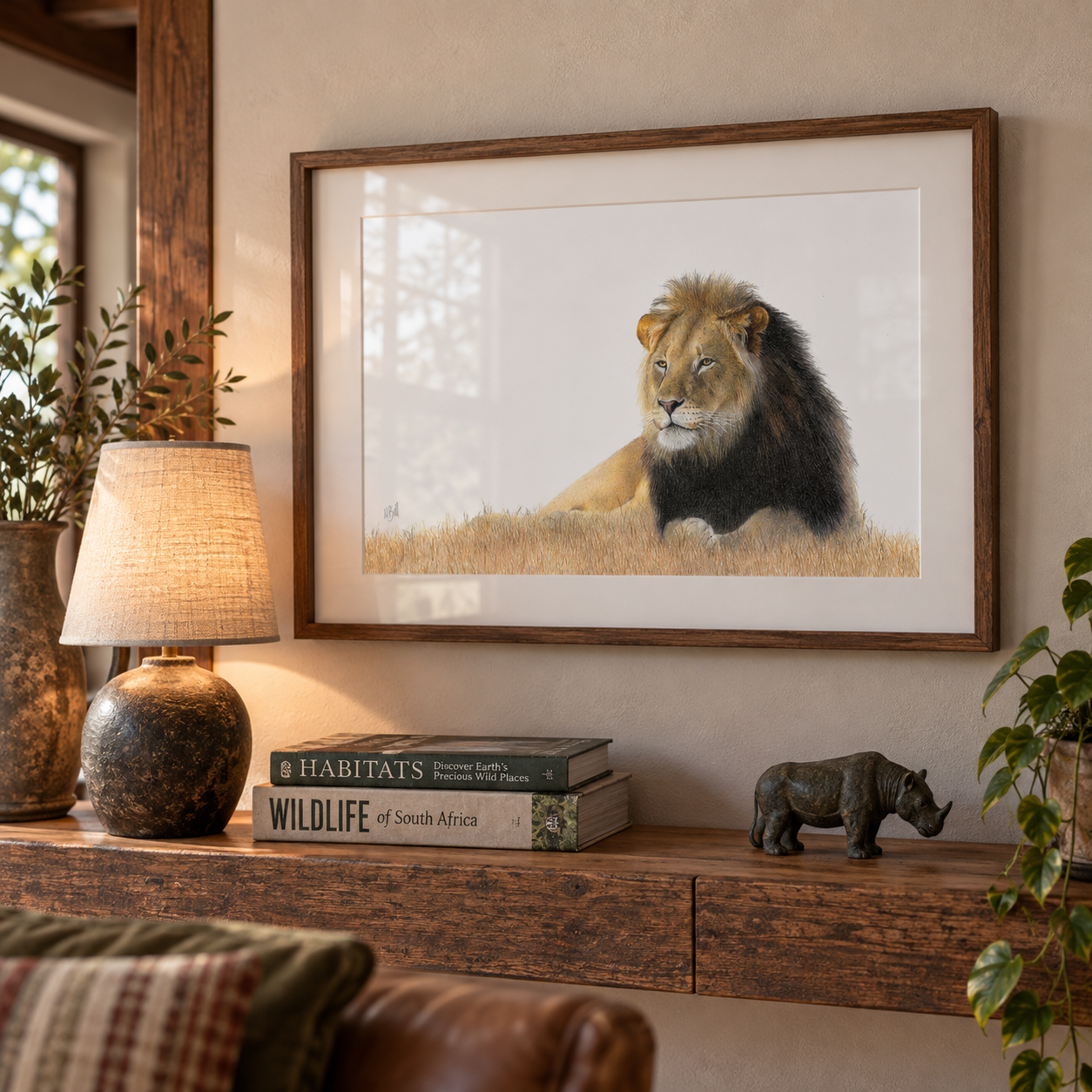 A framed art print of a lion resting in a grassy field, displayed on a wooden console table in a styled living room setting with a lamp, books, and a small rhinoceros figurine.