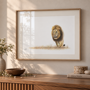 A framed art print depicting a detailed illustration of a male lion walking on a grassy plain, displayed on a wooden console table in a warm, sunlit room.