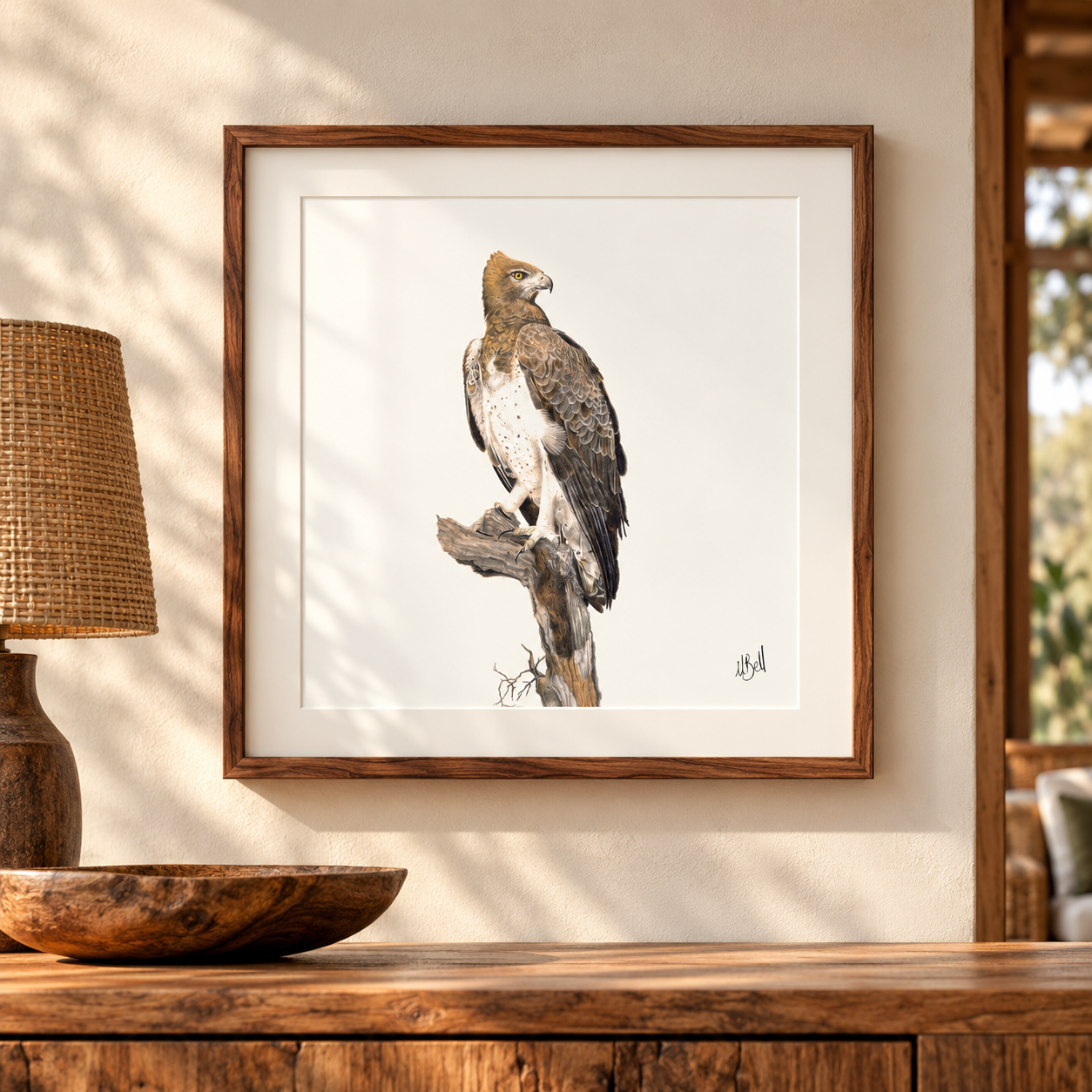 A framed art print of a Martial Eagle perched on a branch, displayed on a wooden console table in a warm, rustic room setting.