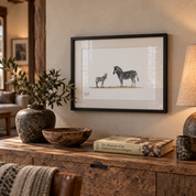 A framed black-and-white zebra art print hangs on a beige wall above a rustic wooden console table styled with a vase, bowl, book, and lamp in a warm, modern interior.