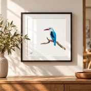 Framed wall art featuring a Woodland Kingfisher bird perched on a branch, displayed in a black frame on a beige wall above a wooden console table with a vase and bowl.